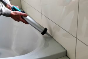 hände mit silikonspritze an badewanne