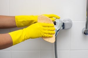 Hände in Putzhandschuhen reinigen Duscharmatur mit Schwamm