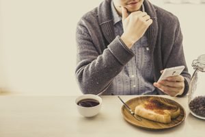 Mann sitzt mit Smartphone beim Essen