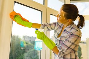 Frau putzt mit Sprühflasche und Lappen Fensterrahmen