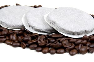 Kaffeepads liegen auf Kaffeebohnen auf weißem Grund