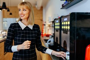 Frau stellt Tasse in Kaffeevollautomat