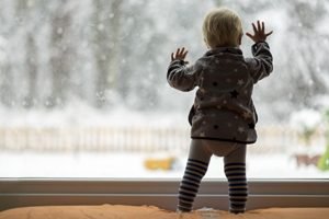 Kleinkind steht an Fenster und fasst gegen die Scheibe