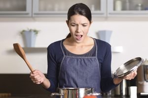 Frau mit Deckel und Löffel blickt fassungslos in Topf