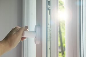 Hand öffnet Fenster mit weißem Rahmen vor Sonne