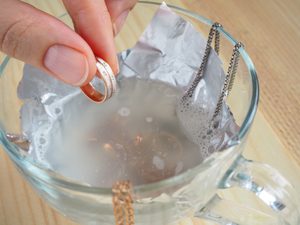 Hand legt Schmuck in Glas mit Wasser und Alufolie