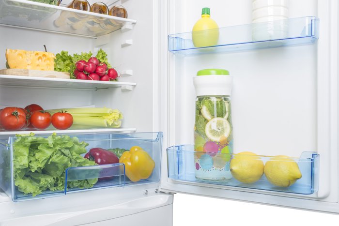 offener, sauberer Kühlschrank mit Gemüse und Zitronenwasser