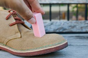 Hand hält einen Radierer auf einen hellen Wildlederschuh