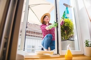 Frau mit Strohhut putzt Glastür auf dem Balkon