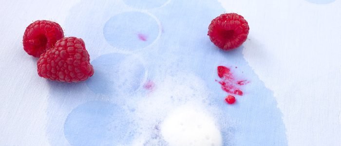 Himbeeren liegen auf einer rotfleckigen hellblauen Tischdecke