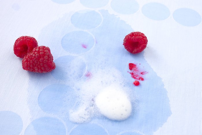 Himbeeren liegen auf einer rotfleckigen hellblauen Tischdecke