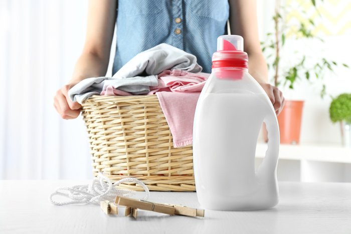 weißes Waschmitte in neutraler Flasche vor einem Wäschekorb