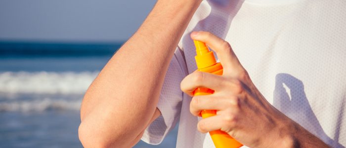 Oberkörper eines Mannes im Shirt mit Sonnencreme vor dem Meer