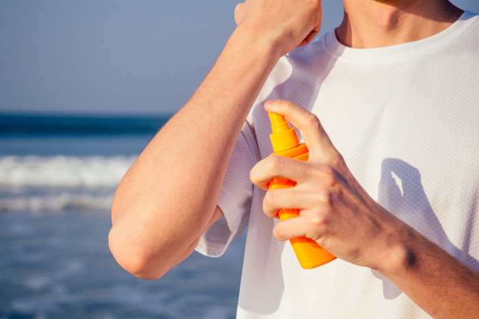Oberkörper eines Mannes im Shirt mit Sonnencreme vor dem Meer
