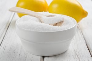 Zitronensäure in Pulverform und Zitronen