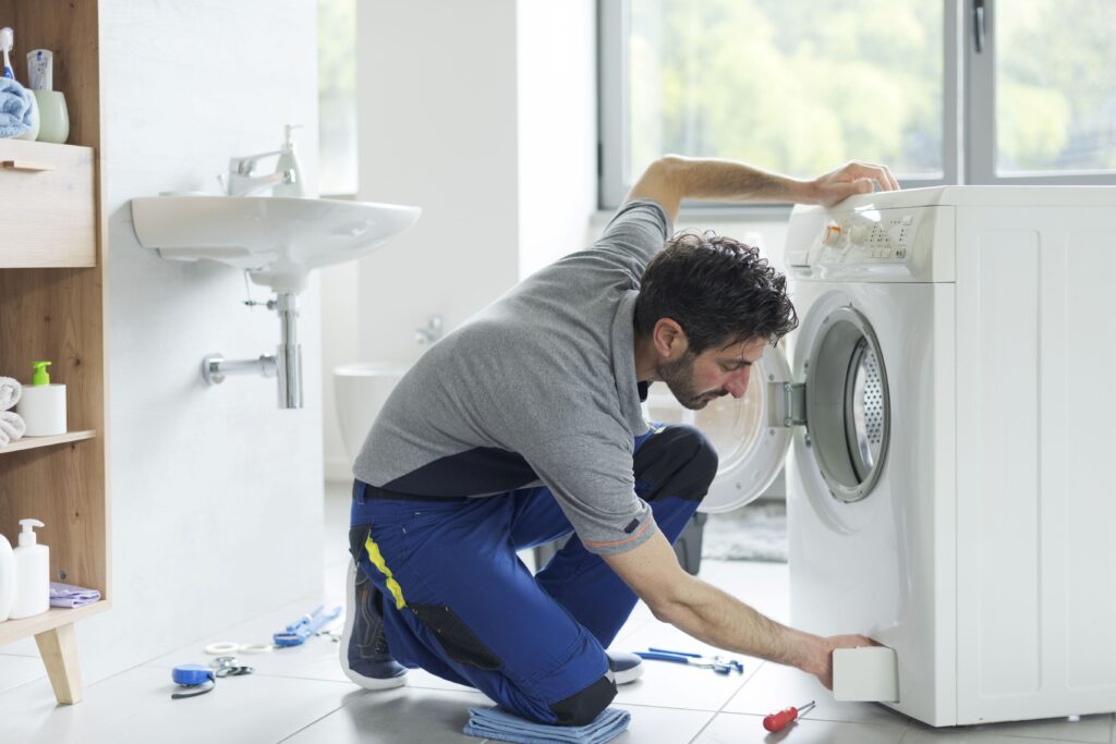 Ein Handwerker kniet vor einer Waschmaschine und überprüft das Flusensieb.